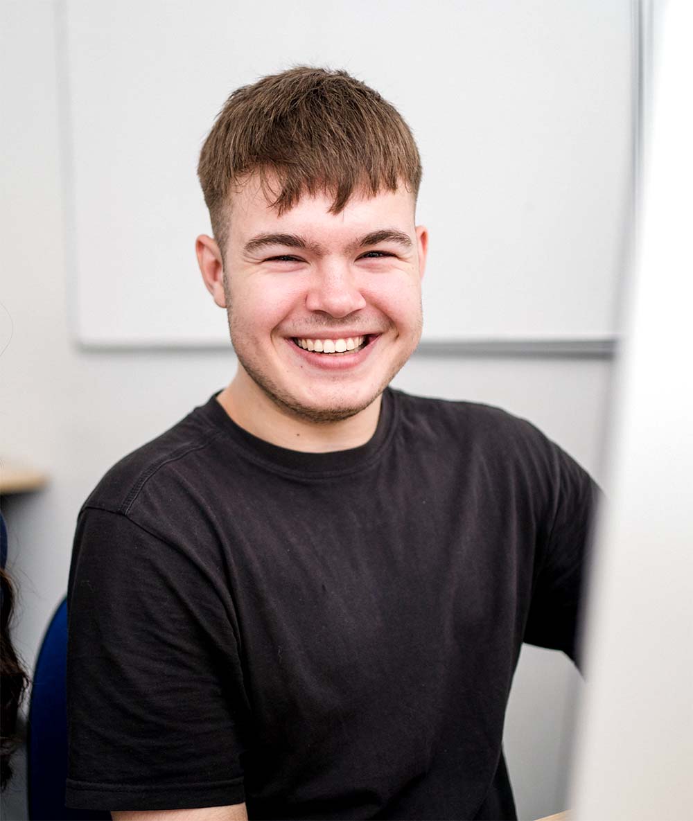 Student wearing black tshirt sat in classroom smiling