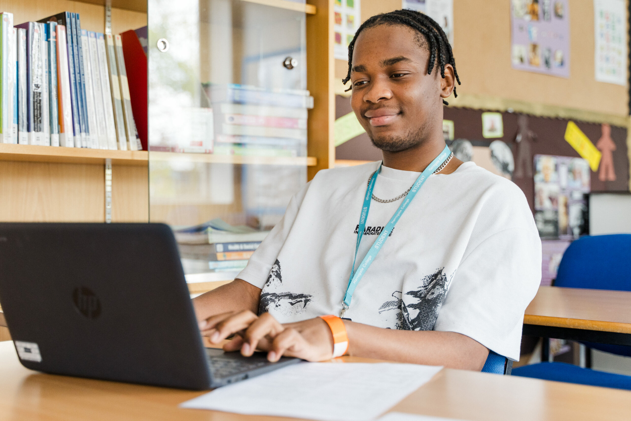 Student wearing blue lanyard sitting in classroom working on laptop
